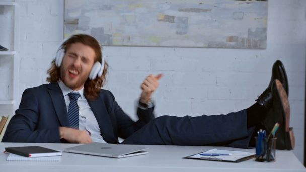 Lockiger Geschäftsmann gestikuliert und hört Musik über Kopfhörer  - Filmmaterial, Video