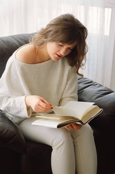 Piękna młoda kobieta czyta książkę w domu. Przemyślana dziewczyna czytająca ważną książkę - Zdjęcie, obraz