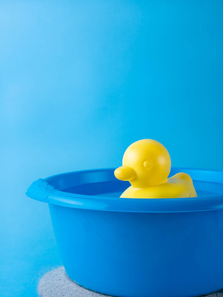 pato de borracha amarelo flutuando em uma tigela de lavagem azul cheia de água, isolado em fundo azul, com espaço de cópia, conceito de férias de verão
 - Foto, Imagem
