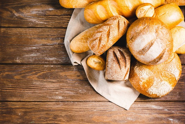 Свежий выпеченный хлеб с золотой корочкой, буханкой, булочками, белым, ржаным на деревенском деревянном фоне с шилом деревенским. Плоская планировка
 - Фото, изображение