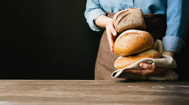 Mulher segura em suas mãos um monte de rolos de pão fresco um fundo escuro. Estilo de padaria caseira rústica. Quadro horizontal
 - Foto, Imagem