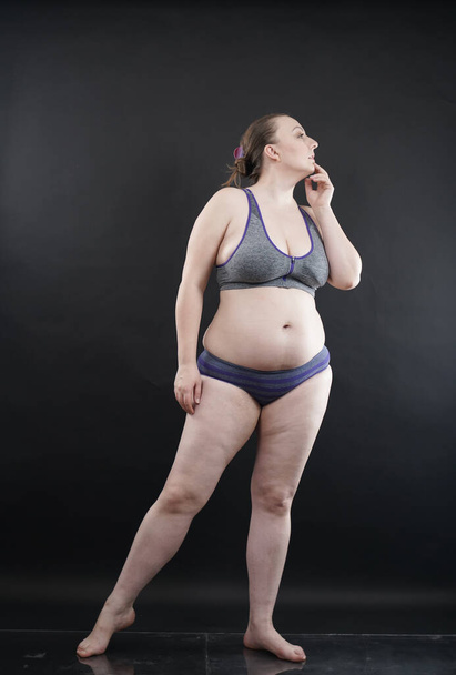 plus size woman shows her body in stretch marks and hair with cellulite and encourages you to love and accept yourself in any way . black background in the Studio. full length photo - Foto, afbeelding