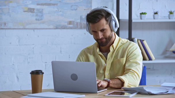 uomo barbuto ascoltare musica in cuffie vicino computer portatile in ufficio
 - Filmati, video