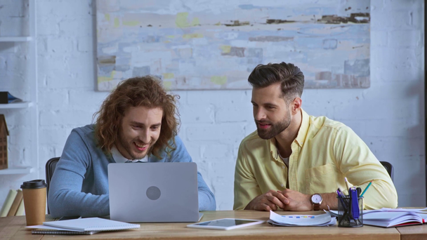 cheerful businessmen looking at laptop near paper cup  - Footage, Video