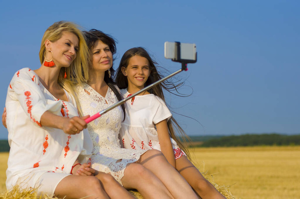 mooie familie nemen een selfie op een hooiberg tegen een blauwe hemel en een tarweveld - Foto, afbeelding