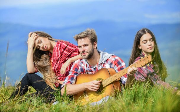 Musical pause. Hiking entertainment. Peaceful place. Melody of nature. Hiking tradition. Friends hiking with music. People relaxing on mountain top while handsome man playing guitar. Singing together - 写真・画像