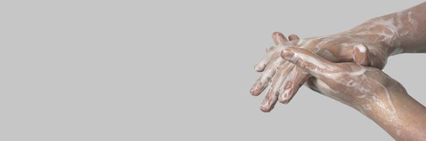 Handen van een jongeman in zeepschuim op een grijze achtergrond. Handwas. Minimale hygiëne, concept van virusbescherming - Foto, afbeelding
