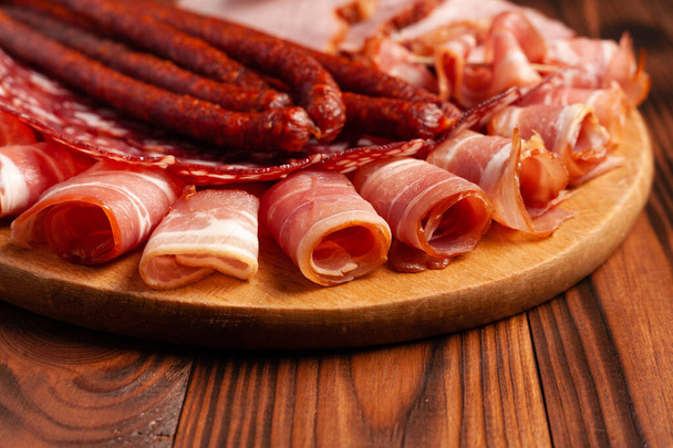 Assorted meat snacks on a wooden cutting board. Sausage, ham, bacon, smoked meats. Stock photo of meat products with blank space. - Фото, зображення