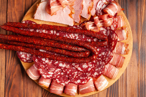 Diverse vleessnacks op een houten snijplank. Worst, ham, spek, gerookt vlees. Stockfoto van vleesproducten met lege ruimte. - Foto, afbeelding
