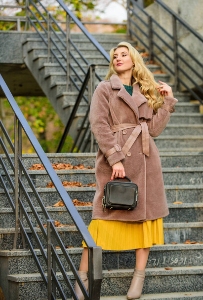 Create fall outfit to feel comfortable and pretty. Autumn outfit. Woman wear stylish outfit and carry purse. Outerwear of modern warm and stylish eco fur. Girl warm coat stand urban stairs background - Φωτογραφία, εικόνα