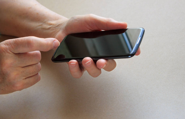 an elderly woman's hands hold a dark-colored cell phone, a concept for teaching an adult new technologies - Φωτογραφία, εικόνα
