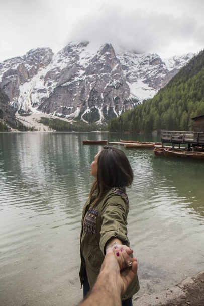 brunette woman with green jacket shakes hands with her partner and shows us the stunning landscape of Lake Braies, greenish lake, snowy mountains and - Fotoğraf, Görsel