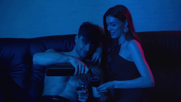 shirtless man pouring wine in glass of beautiful girlfriend on blue - Footage, Video