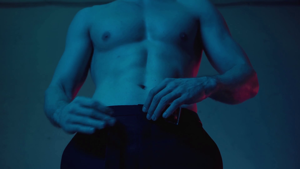vue recadrée de l'homme sexy et musclé se déshabiller sur bleu - Séquence, vidéo