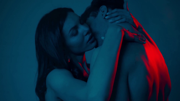 Όμορφος άντρας φιλάει ελκυστική γυναίκα απομονωμένη στο μπλε - Πλάνα, βίντεο