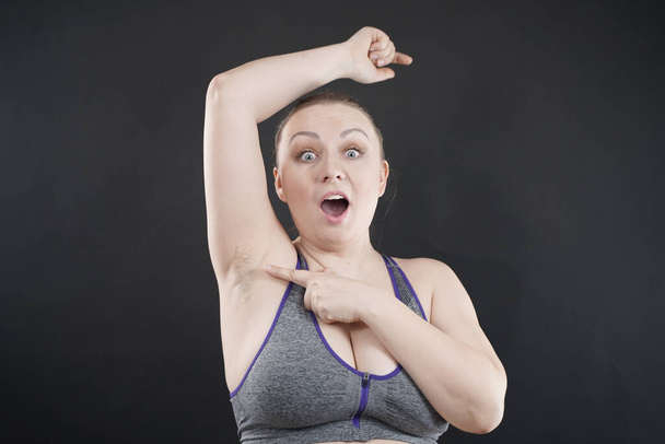 young happy plus size caucasian woman shows her unshaved armpit on black studio background - Photo, image