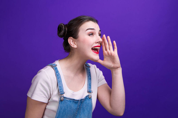 Portrait of beautiful young woman calling for someone with hand on her mouth over purple background - Foto, Imagem