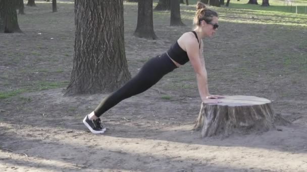 Push ups ή press ups άσκηση από νεαρή γυναίκα. Νεαρή γυναίκα κάνει πους απς στο δάσος. Γυναίκα αθλητής που κάνει ασκήσεις για τους μυς των χεριών push-ups από ένα κομμένο δέντρο σε ένα πάρκο - Πλάνα, βίντεο