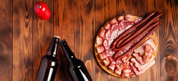 Μπύρα σνακ με τη μορφή προϊόντων κρέατος και εμφιαλωμένης μπύρας. Ορεκτικό σε μορφή τεμαχισμού μπέικον, σαλαμιού, ζαμπόν, κυνηγετικών λουκάνικων. Στοκ φωτογραφία μπύρα και σνακ σε ένα ξύλινο τραπέζι. - Φωτογραφία, εικόνα