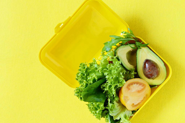 Lunchbox mit einem Snack aus Salat, Tomate, Avocado auf gelbem Hintergrund. Konzept für gesunde Ernährung. Gehen Sie vegan. Leckeres vegetarisches Essen in Plastikbox. - Foto, Bild