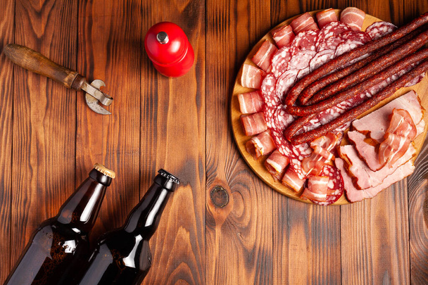 Beer snack in the form of meat products and bottled beer. Appetizer in the form of slicing bacon, salami, ham, hunting sausages. Stock photo beer and snack on a wooden table. - Photo, Image