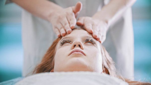 Massaggio massaggiatrice impastare la zona della fronte ad una giovane donna con i palmi delle mani
 - Foto, immagini