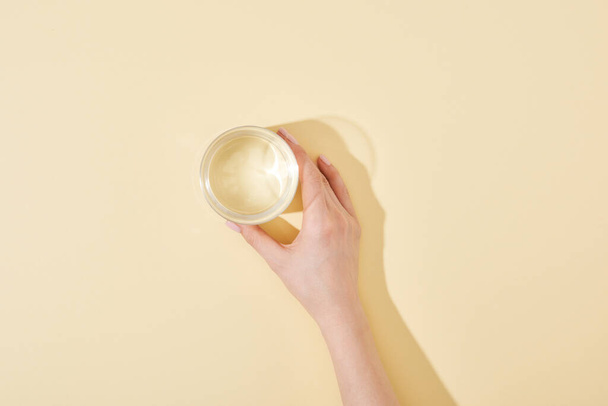 cropped view of woman holding glass of water on beige background - Fotografie, Obrázek