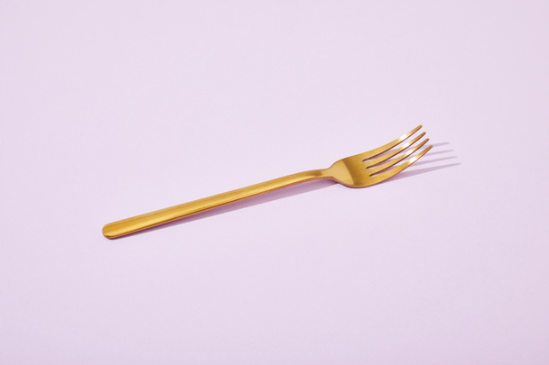 metallisch glänzende goldene Gabel auf violettem Hintergrund - Foto, Bild