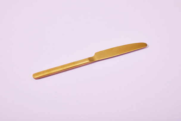 metal shiny golden knife on violet background - 写真・画像