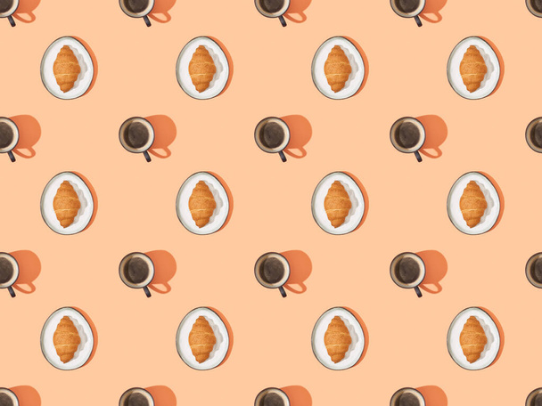 top view of fresh croissants on plates and coffee on orange, seamless background pattern - Zdjęcie, obraz