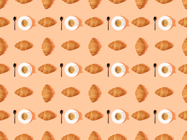 top view of spoons, fresh croissants on plates and coffee on orange, seamless background pattern - 写真・画像