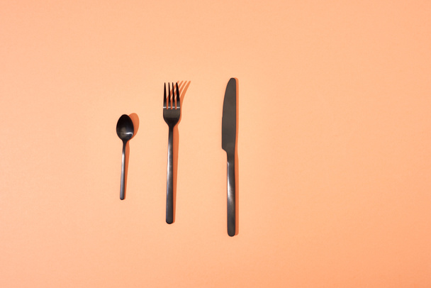 top view of metal shiny black fork, spoon and knife on orange background - Valokuva, kuva