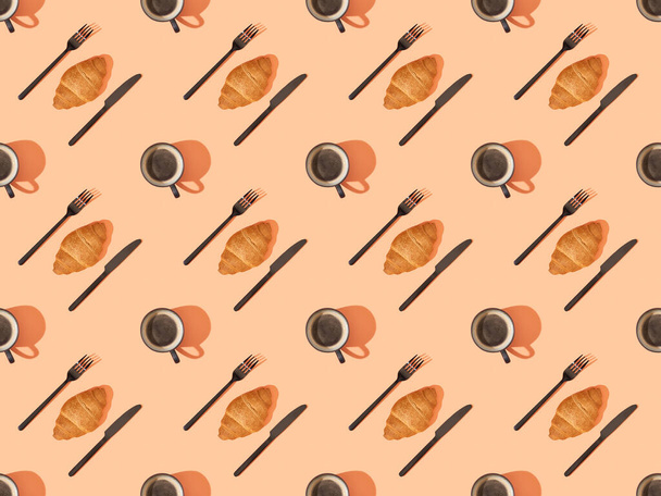 top view of cutlery, fresh croissants and coffee on orange, seamless background pattern - Photo, Image