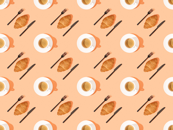top view of cutlery, fresh croissants on plates and coffee on orange, seamless background pattern - Photo, Image