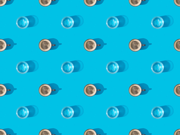 top view of cups of fresh coffee and glasses of water on blue, seamless background pattern - Photo, image