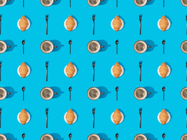 top view of cutlery, croissants on plates and coffee on blue, seamless background pattern - 写真・画像
