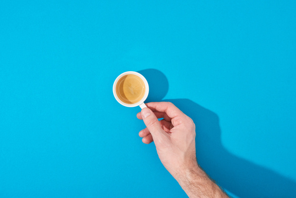 cropped view of man holding cup of fresh coffee on blue background - Fotó, kép
