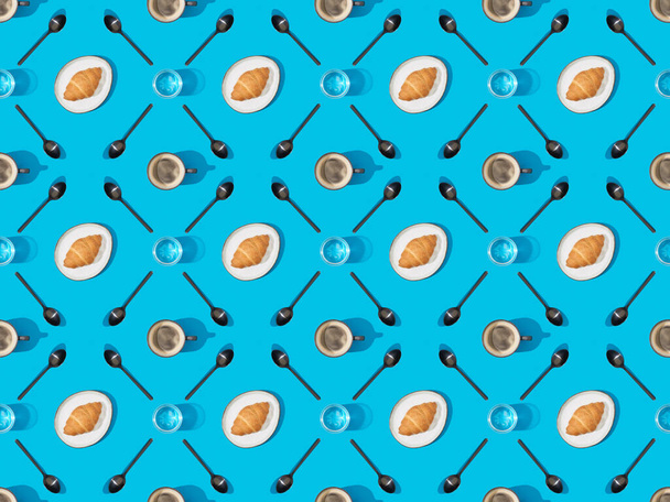 top view of spoons, croissants on plates, water and coffee on blue, seamless background pattern - Foto, afbeelding