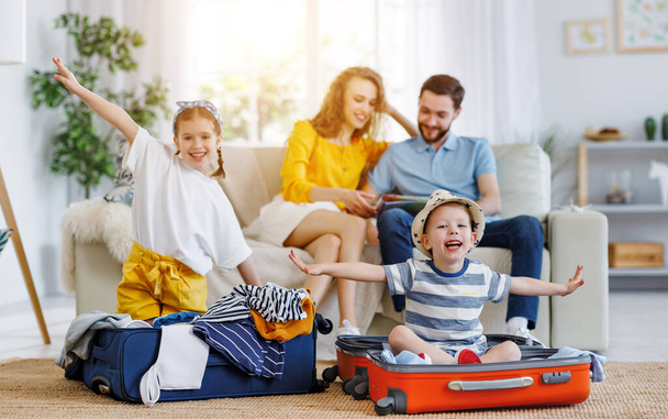 Laughing siblings sitting in suitcases on floor holding hands apart in flight anticipating journey with loving parents sitting on sofa on backgroun - Foto, Bild