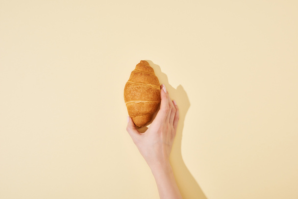 vista cortada de mulher segurando croissant fresco no fundo bege
 - Foto, Imagem