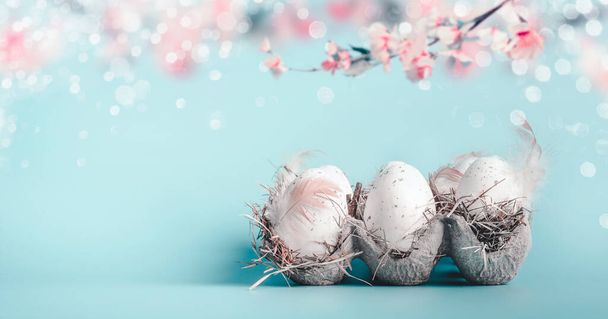 Easter background in pastel color. Egg-crate with Easter eggs at blue with bokeh and hanging spring blossom branches, front view with copy space for your design, banner - Photo, image