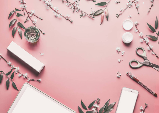 Okostelefon és tabletta pc gúnyolódik pasztell rózsaszín asztali háttér modern kozmetikumok, írószer rugalmasság és virágos ágak, felső nézet. Szépségblog és női üzleti koncepció. Lapos fektetési keret - Fotó, kép