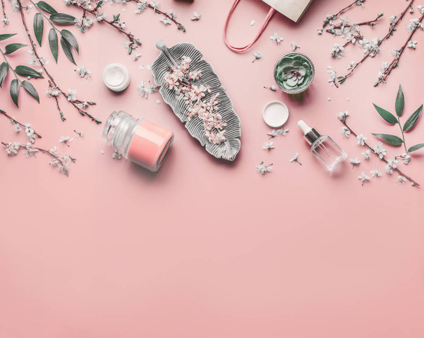 Cosmetic and skin care concept. Various facial anti-aging products on pastel pink background with cherry blossom and leaves, top view, frame. Copy space for your design. Beauty blog layout. Flat lay - Φωτογραφία, εικόνα