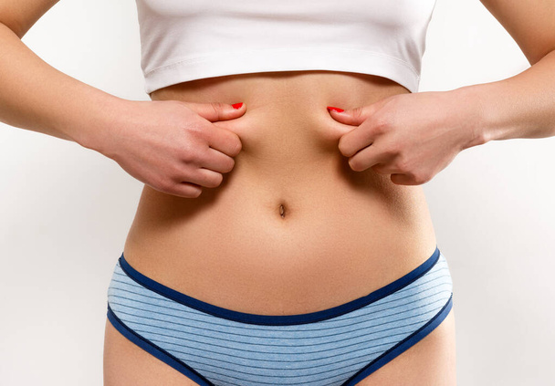 the woman pinches the excess fat on her sides and belly with her fingers. On a white background, close-up - Foto, Imagem