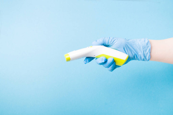 infrared non-contact temperature thermometer in hand, hand in a blue medical glove, instantly measure temperature, blue background copy space, quarantine 2020 - Φωτογραφία, εικόνα