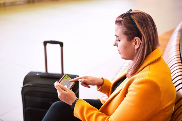 Όμορφη νεαρή γυναίκα Ευρωπαίος ταξιδιώτης (επιβάτης) με ένα smartphone στο χέρι περιμένει την αναχώρηση (πτήση) στο Διεθνές Αεροδρόμιο Havalimani της Κωνσταντινούπολης (IST Airport) - Φωτογραφία, εικόνα