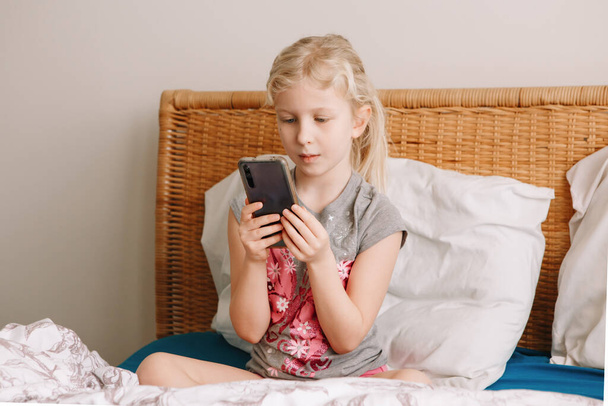 Cute adorable Caucasian girl stay at home and call her friends on smartphone. Child kid having face time call talk with people relatives while on self isolation during quarantine of COVID-19. - Φωτογραφία, εικόνα