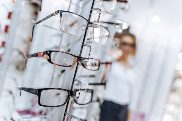 Optical shop. Optician suggest glasses. Woman standing with many eyeglasses in background. - Foto, Imagem