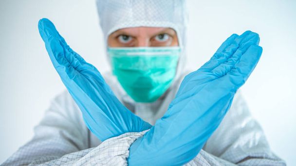 Een blanke man in een beschermend pak en masker toont het stop corona virus teken. Biologisch gevaar. Epidemie van het Chinese coronavirus. Pandemische COVID-19. Begrip "medische en gezondheidszorg" - Foto, afbeelding