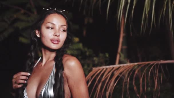 Cute and sexy brunette girl in silver bikini top, denim shorts and sunglasses dancing, smiling, flirting during summer evening - video in slow motion - Materiał filmowy, wideo